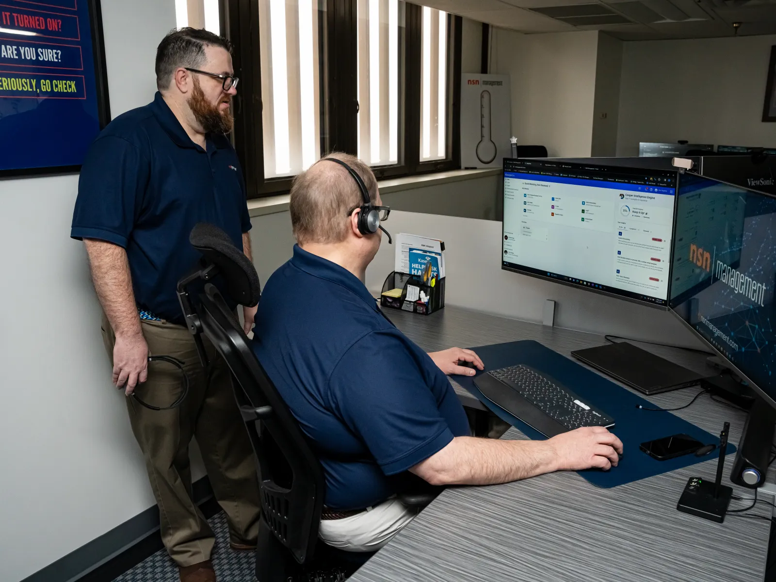 a man sitting at a desk with a man standing next to him