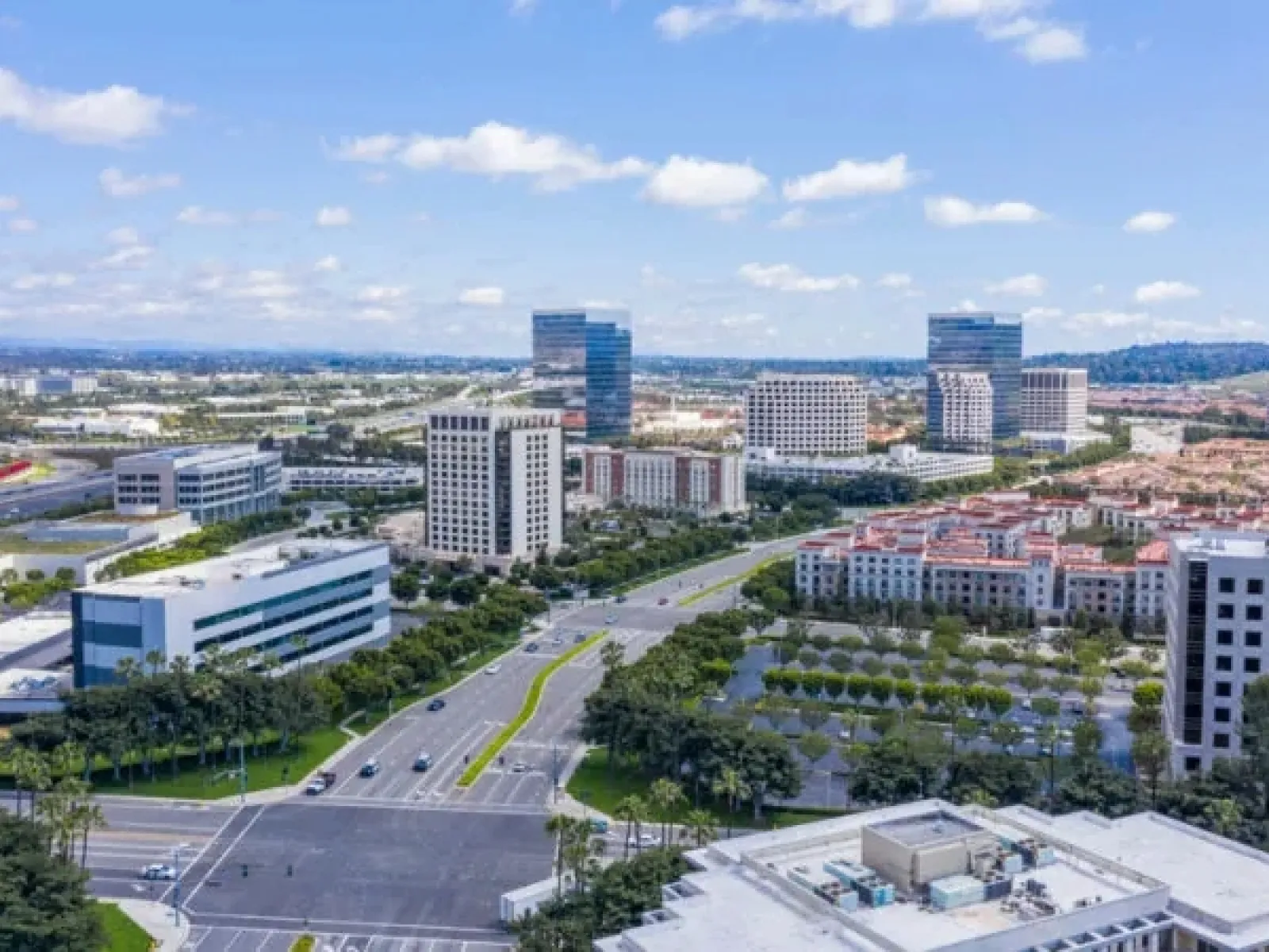 Aerial view of a modern business district with office buildings, roads, trees, and clear blue skies.