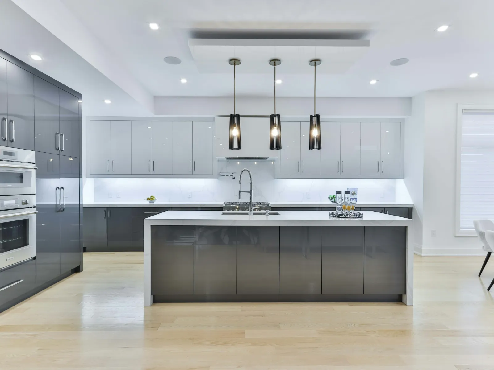 Modern kitchen with gray and white cabinets, central island, pendant lights, built-in oven, and light wood flooring