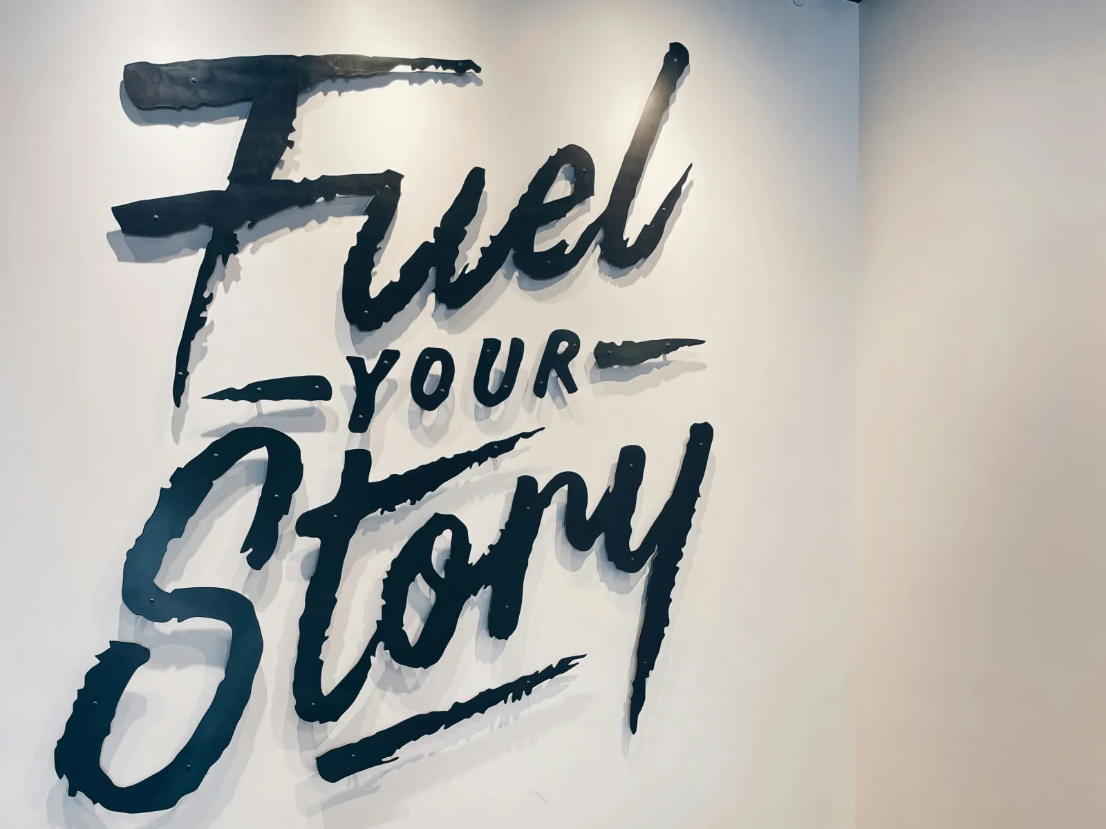 Modern seating area with two black leather chairs and a round wooden table under a Fuel Your Story wall sign.