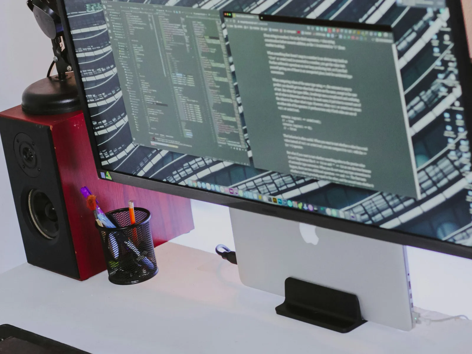 Modern workspace with ultra-wide monitor displaying coding and text, keyboard, mouse, and desk lamp on white desk.