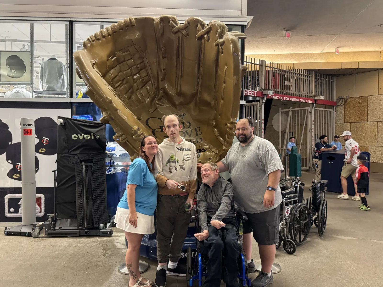 Group of four people posing in front of an oversized baseball glove statue inside a sports venue.