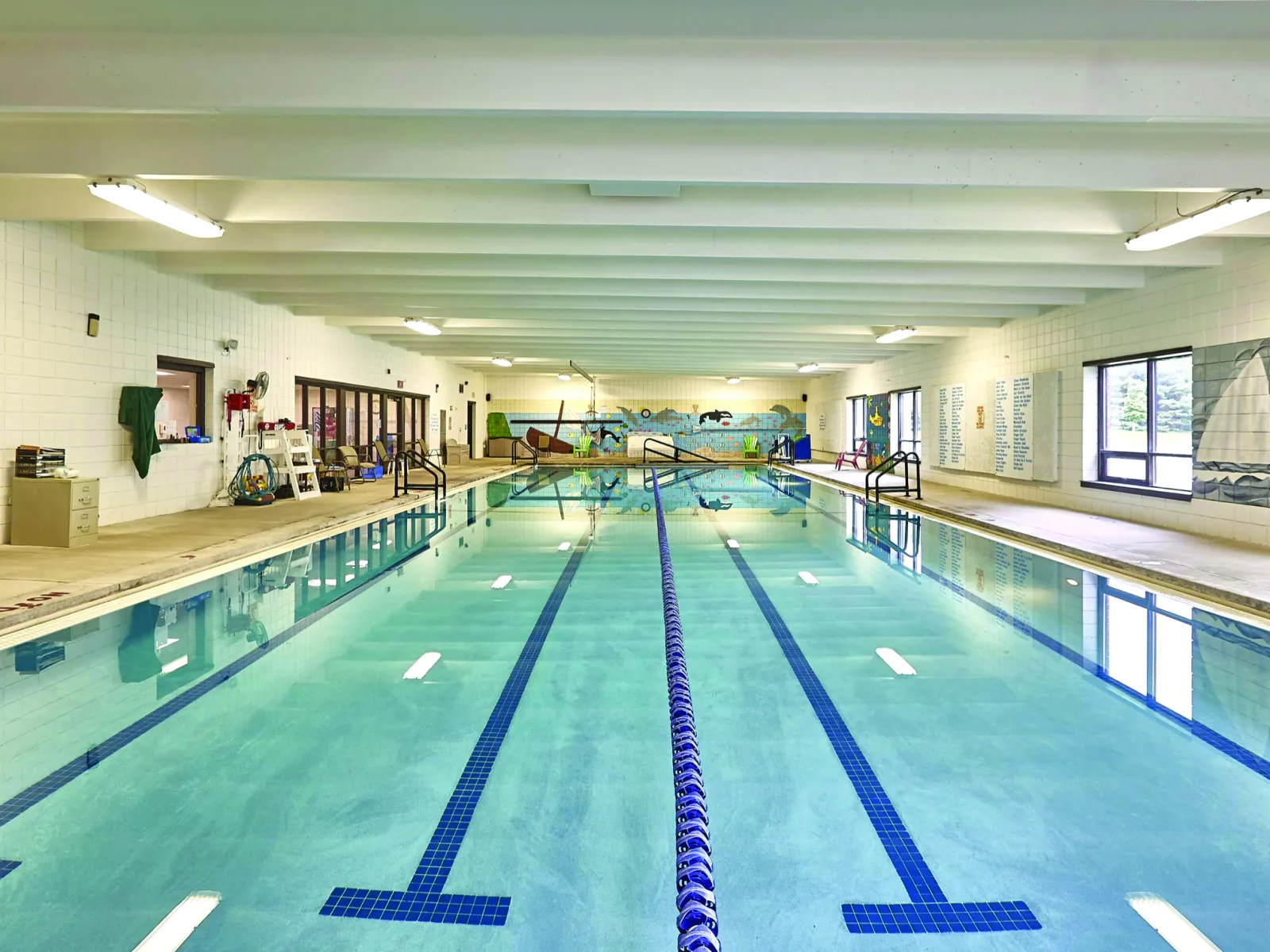 Indoor swimming pool with lane markers, bright lights, and mural along the wall.