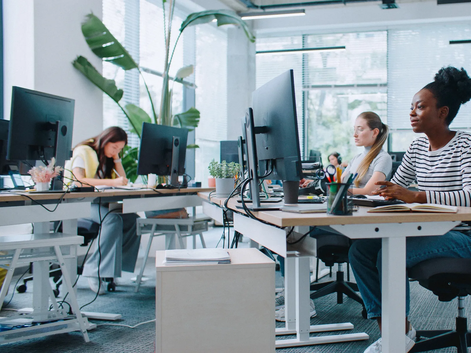 Women working collaboratively in a modern office space with computers and plants.