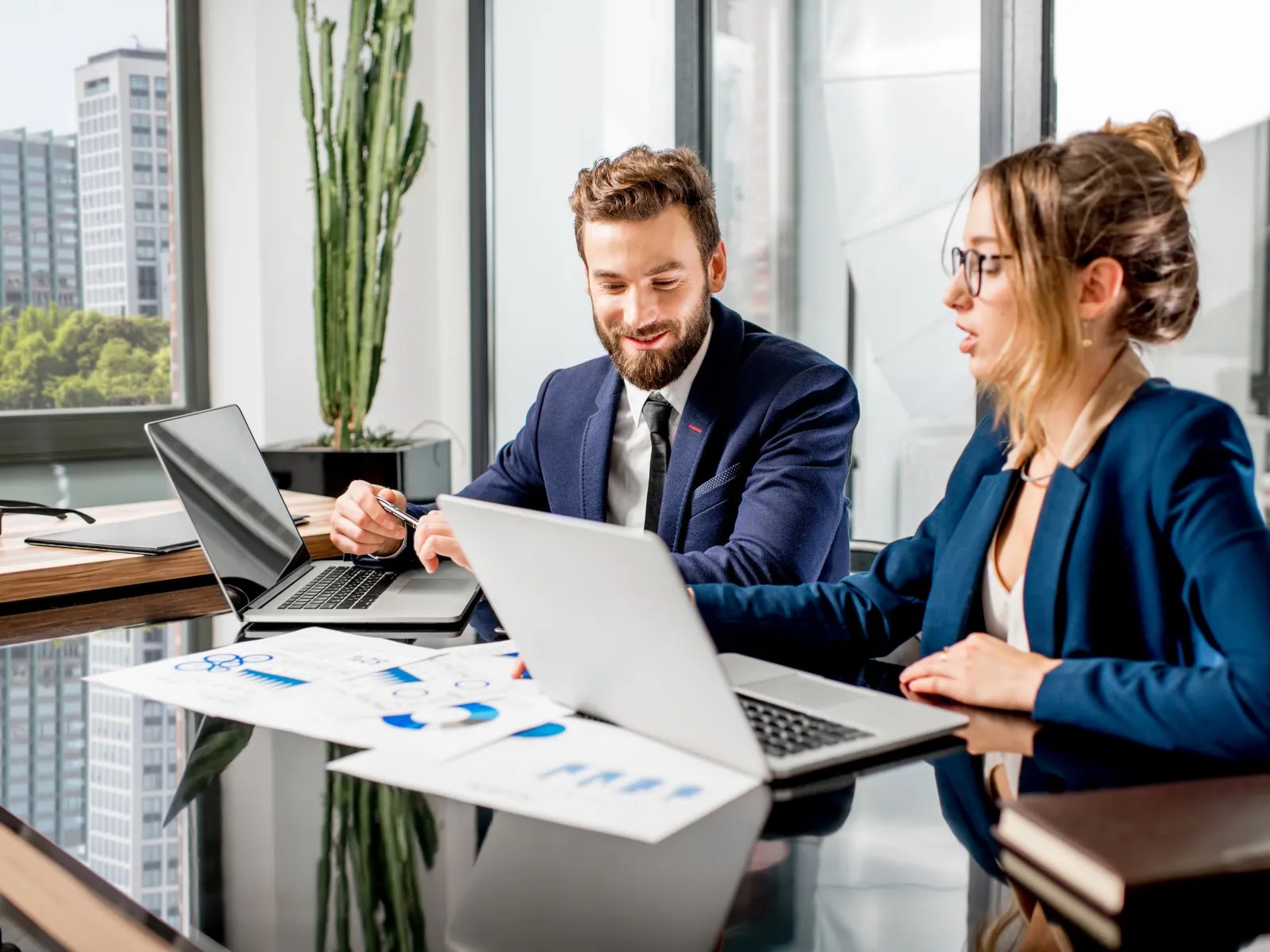 Business professionals collaborating in a modern office with laptops and documents on a glass table.
