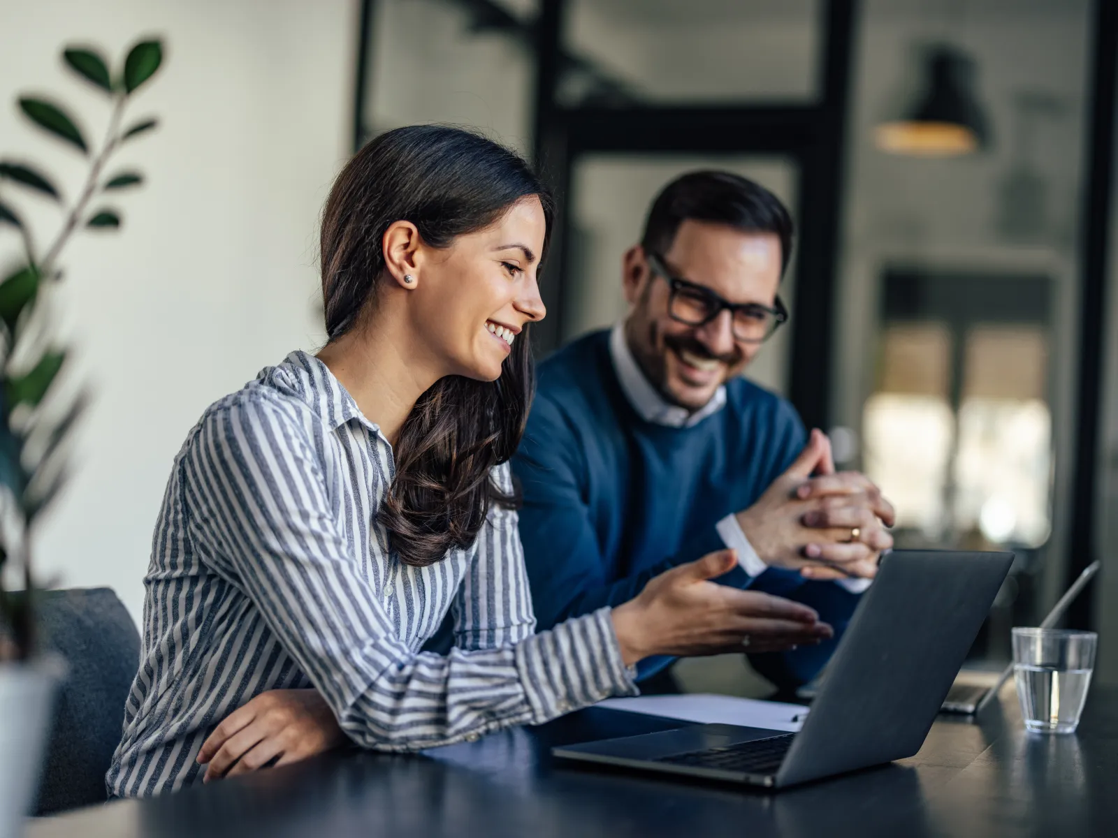 Two professionals collaborating at a desk with a laptop in a modern office setting.