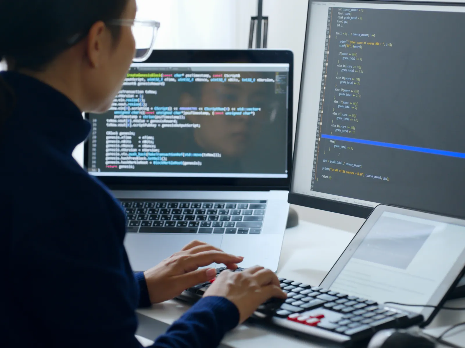 Person coding on multiple screens with laptop and tablet showing programming text and development environment.