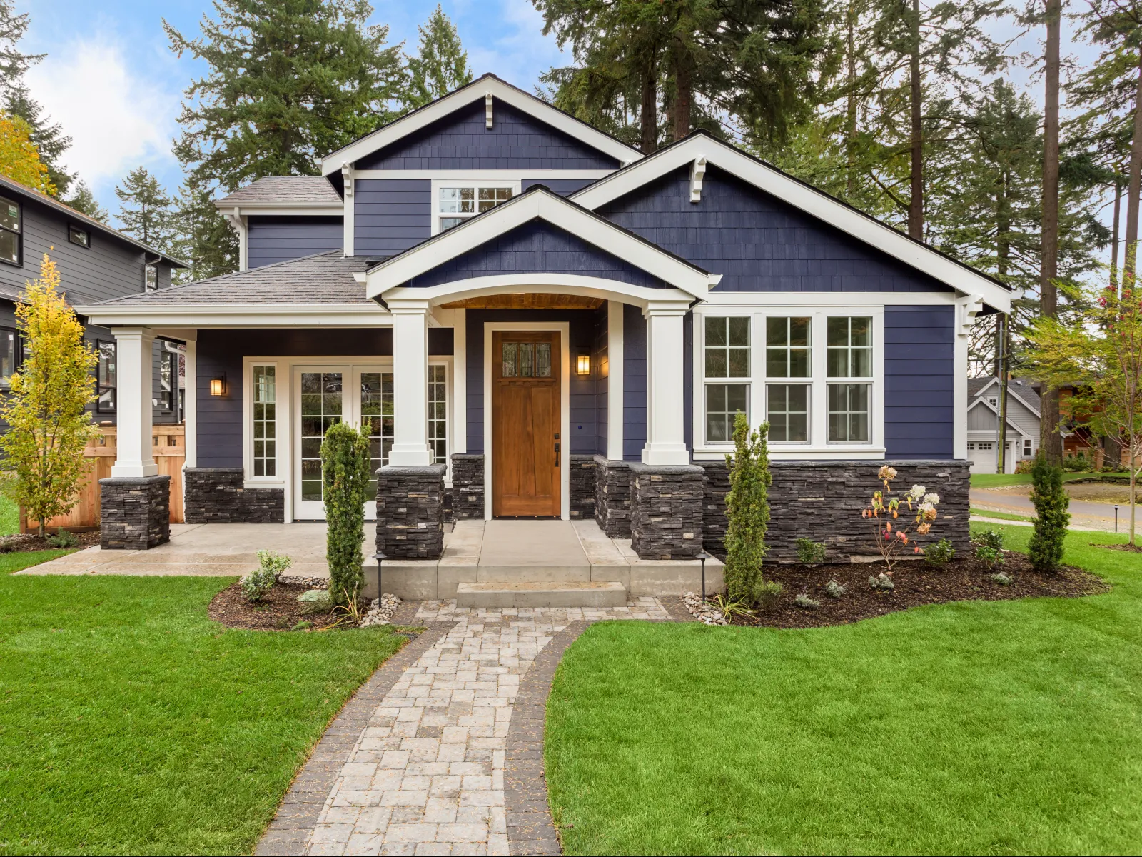 Stylish blue modern house with stone accents and lush green landscaping in a serene neighborhood.