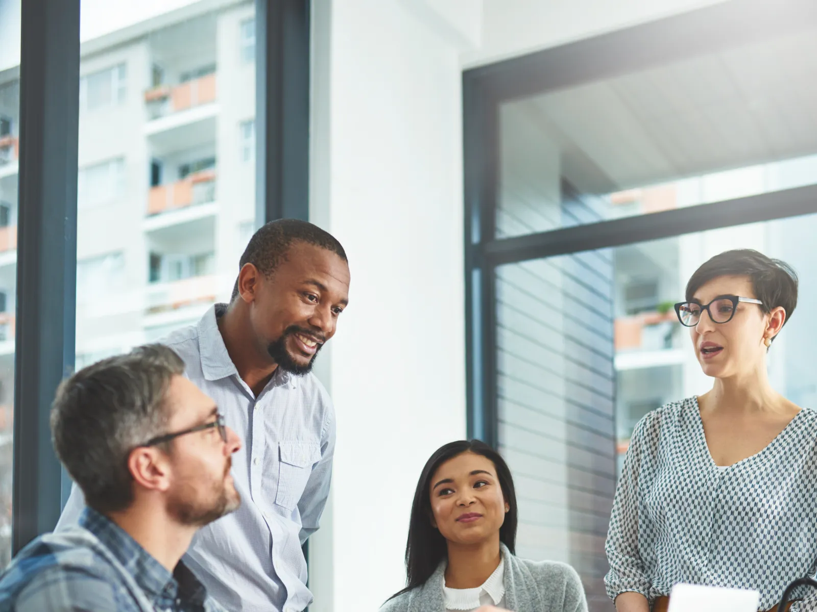 A diverse group of professionals collaborating in a modern office setting around a laptop.