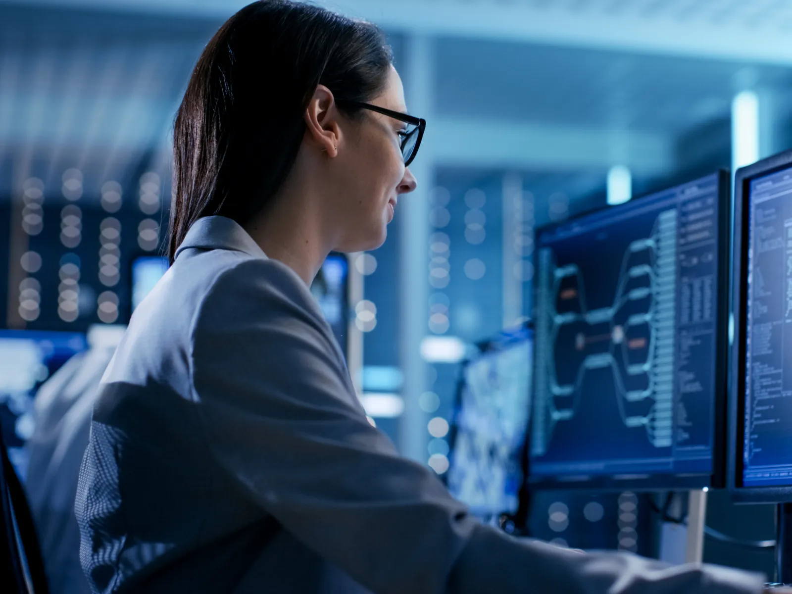 Professional woman working on multiple computer screens in a modern office environment.