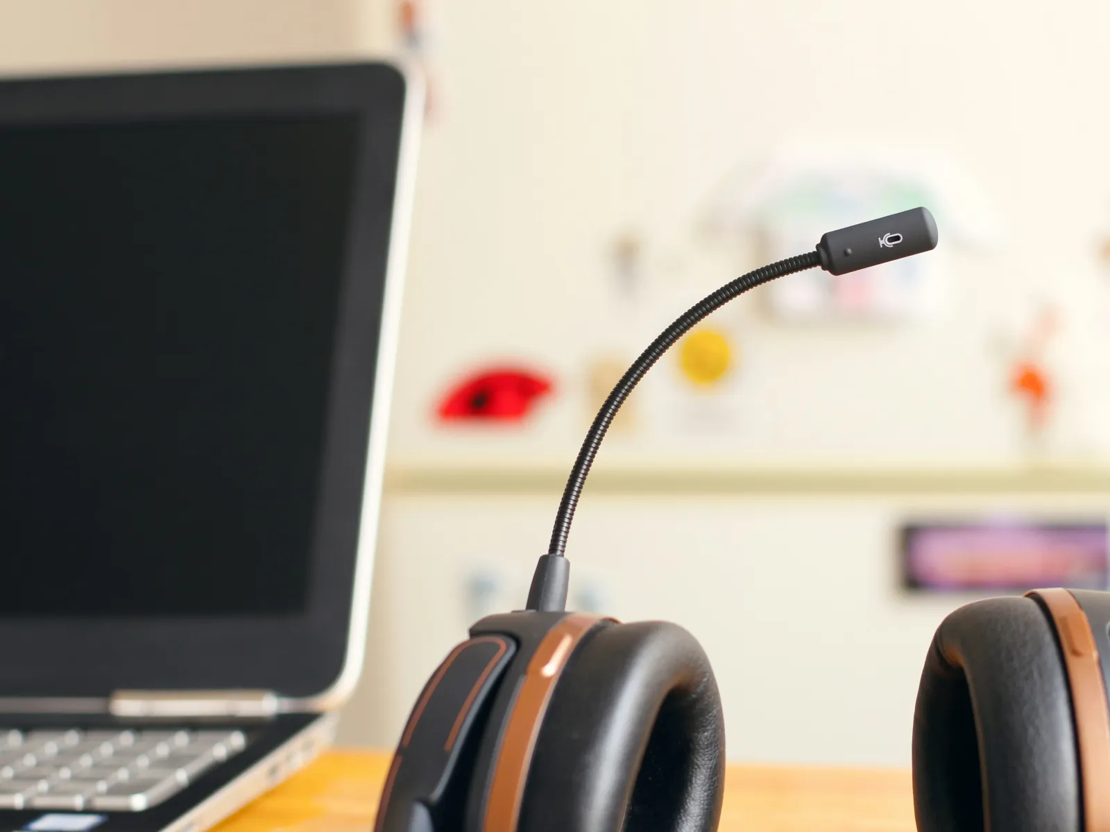 Black over-ear headset with adjustable microphone beside open laptop on wooden desk.