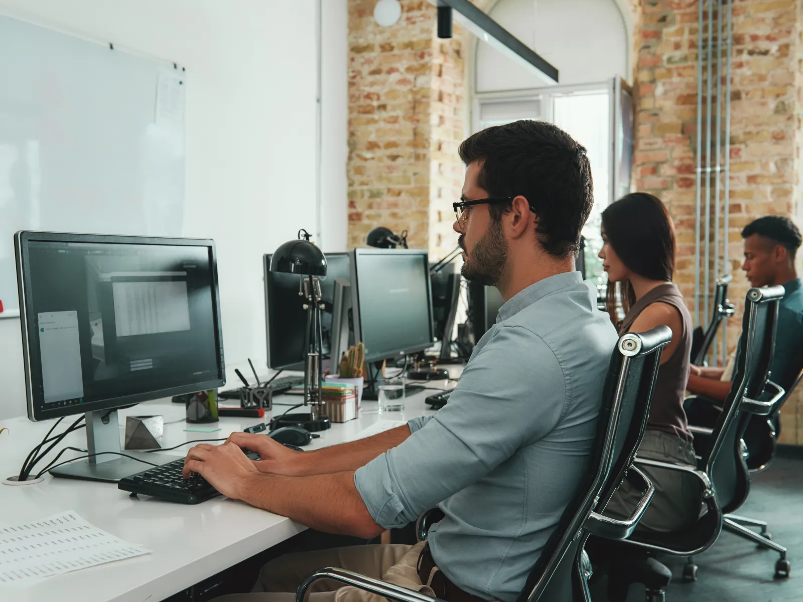Young professionals working on computers in a modern office with exposed brick walls and large windows