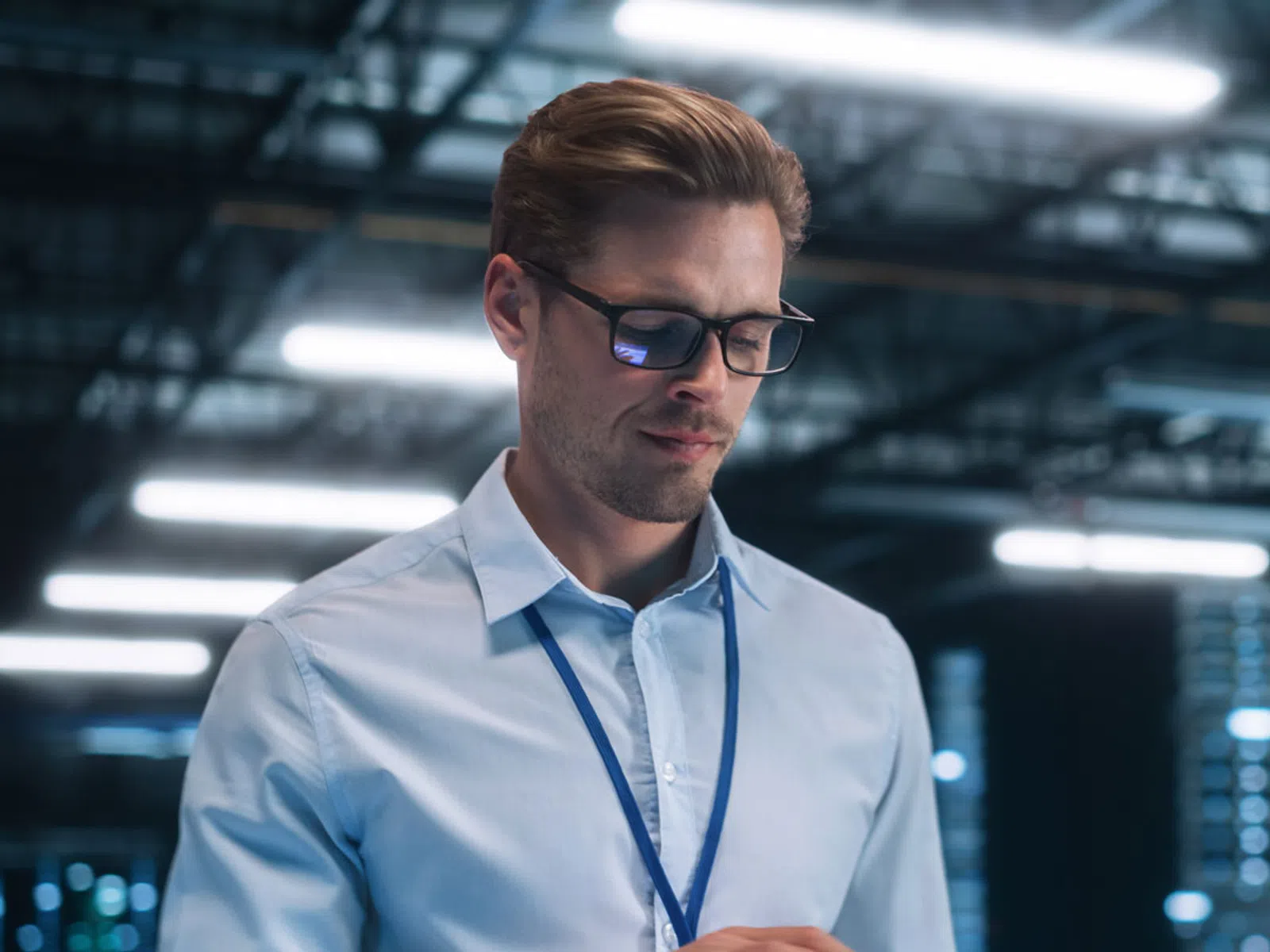 Man in glasses using tablet in a high-tech data center with server racks and bright lighting.