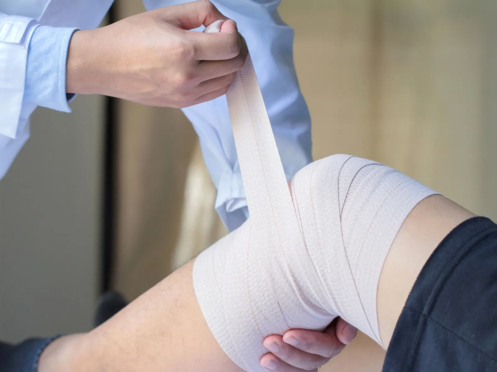 Medical professional wrapping elastic bandage around patient's knee for injury support and treatment.