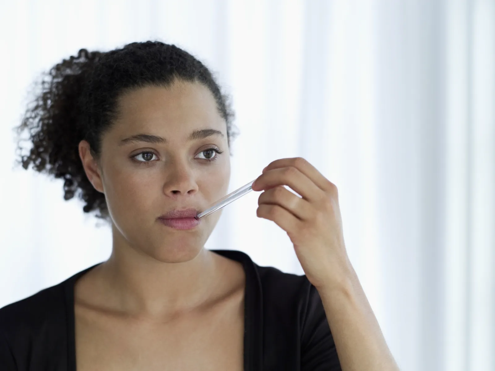 Young woman in black top applying lip balm or gloss to her lips with a clear applicator in natural light.