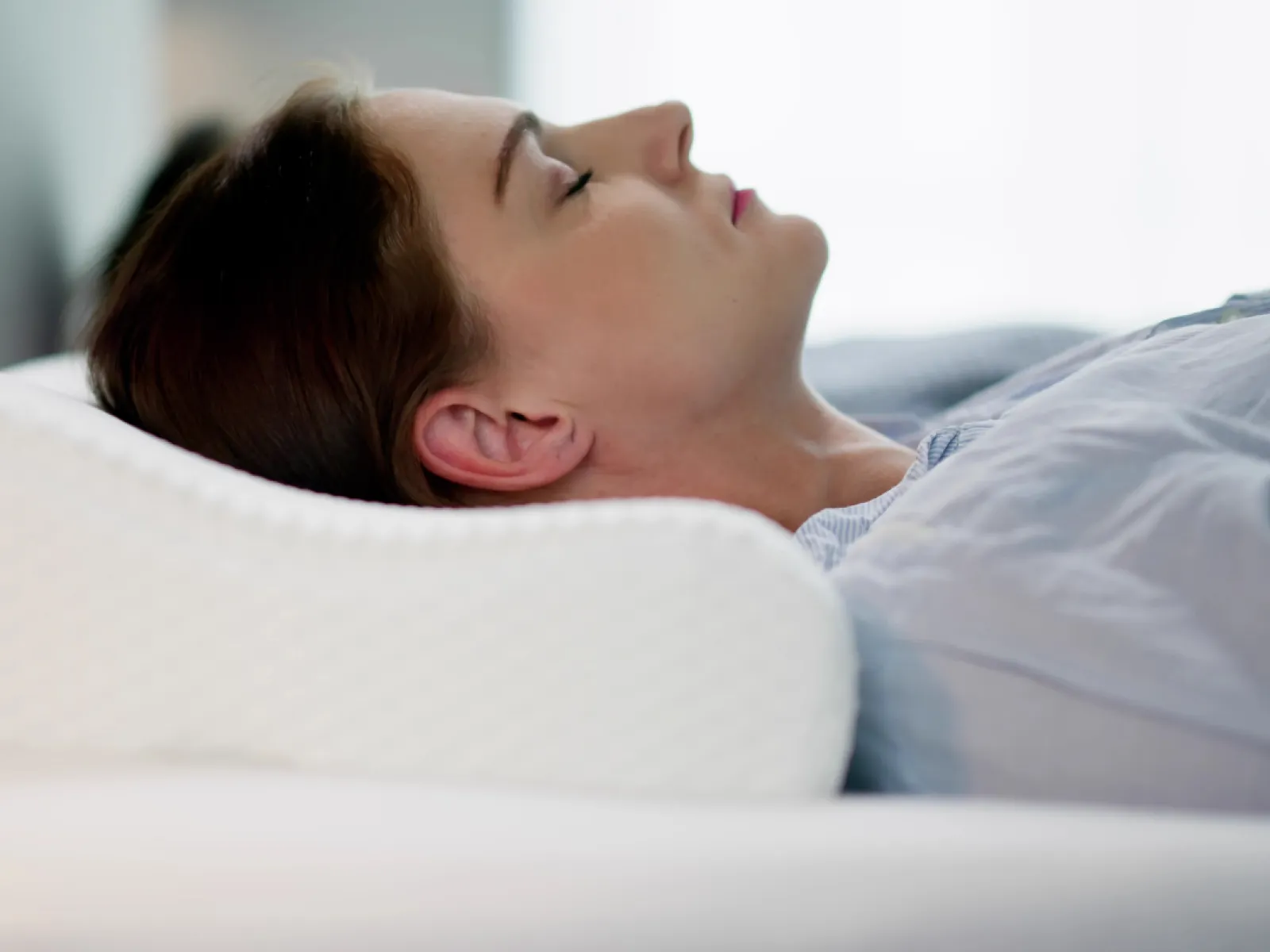 Woman sleeping peacefully on a white ergonomic pillow with soft natural light in the background