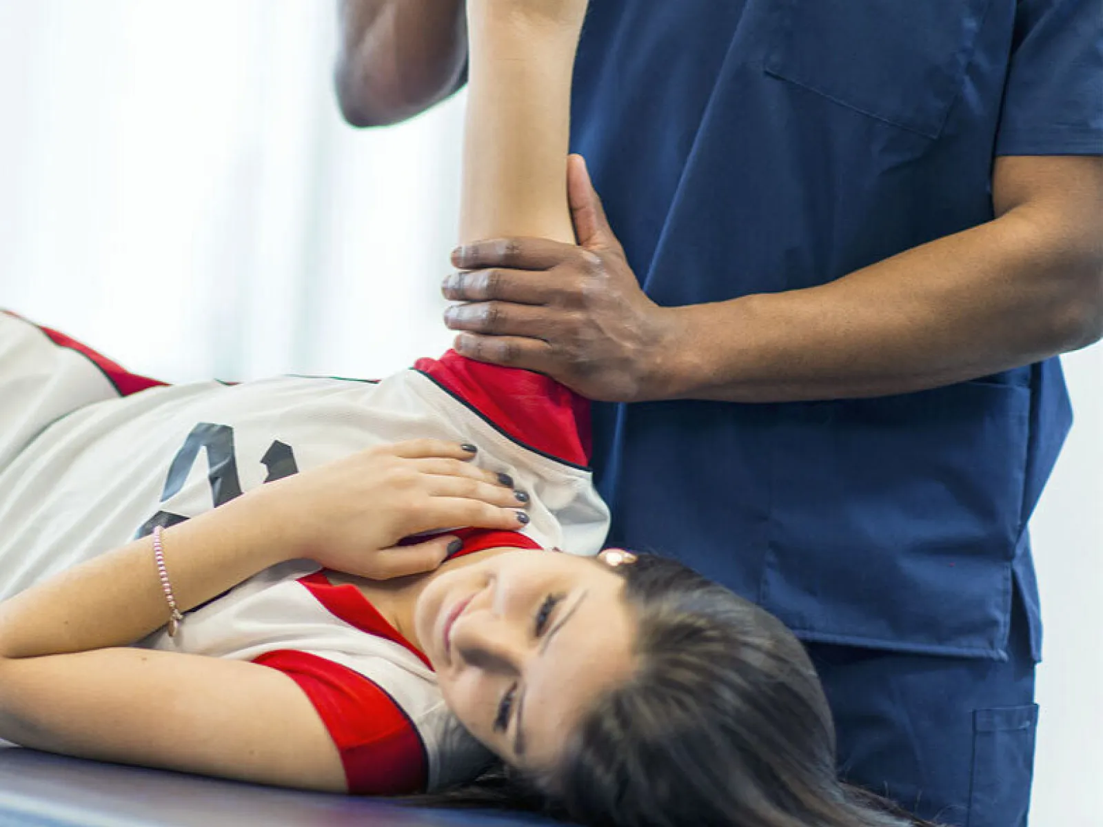 Physical therapist in blue scrubs assisting female athlete with arm stretch on therapy table