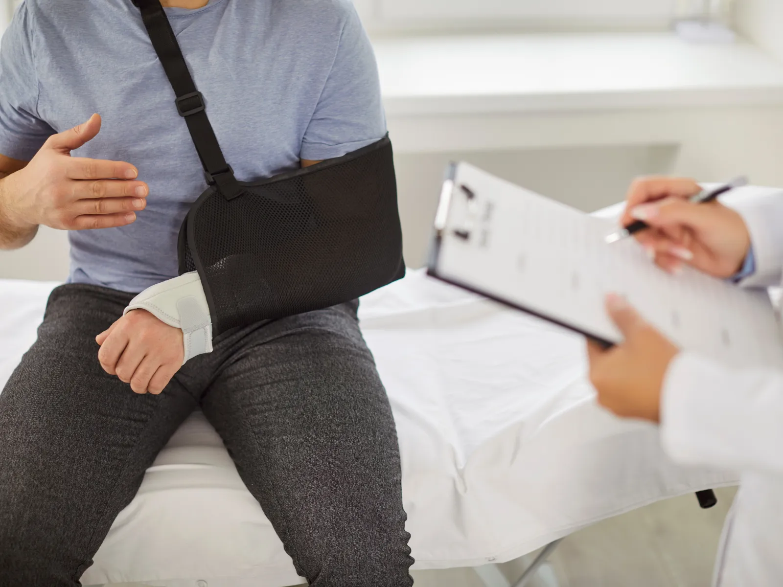Man with arm in sling consulting doctor taking notes on clipboard in medical office.