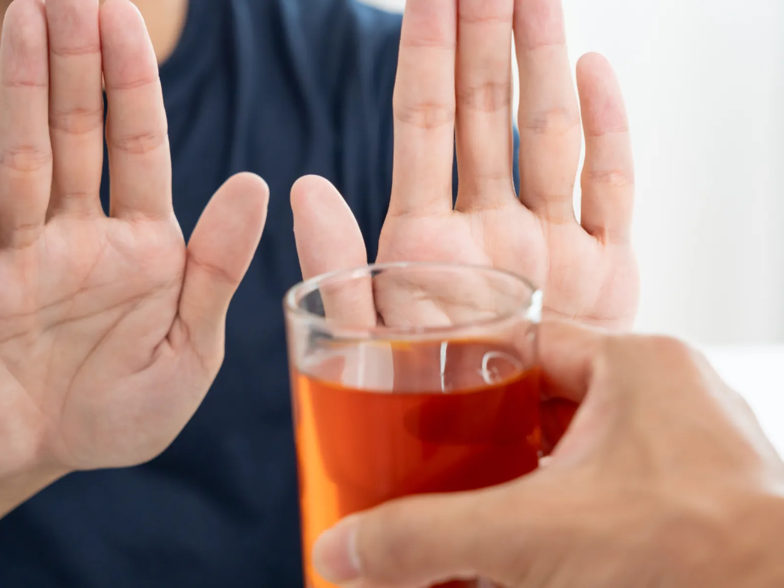 Person refusing a glass of tea with hands raised in a stop gesture against a blurred background.