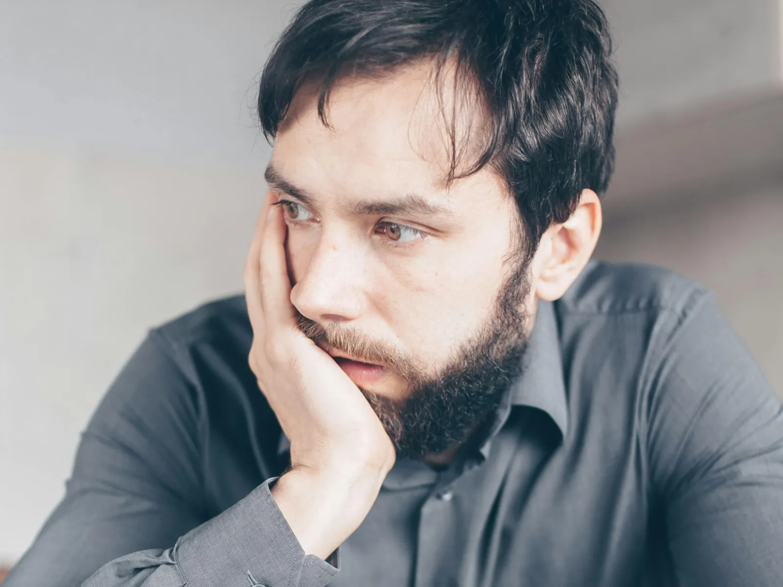Tired young man rubbing eyes while holding glasses sitting in front of laptop at desk
