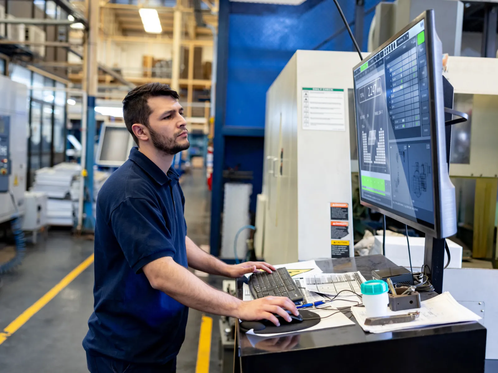 Worker monitoring machine operations on a computer in a manufacturing facility.
