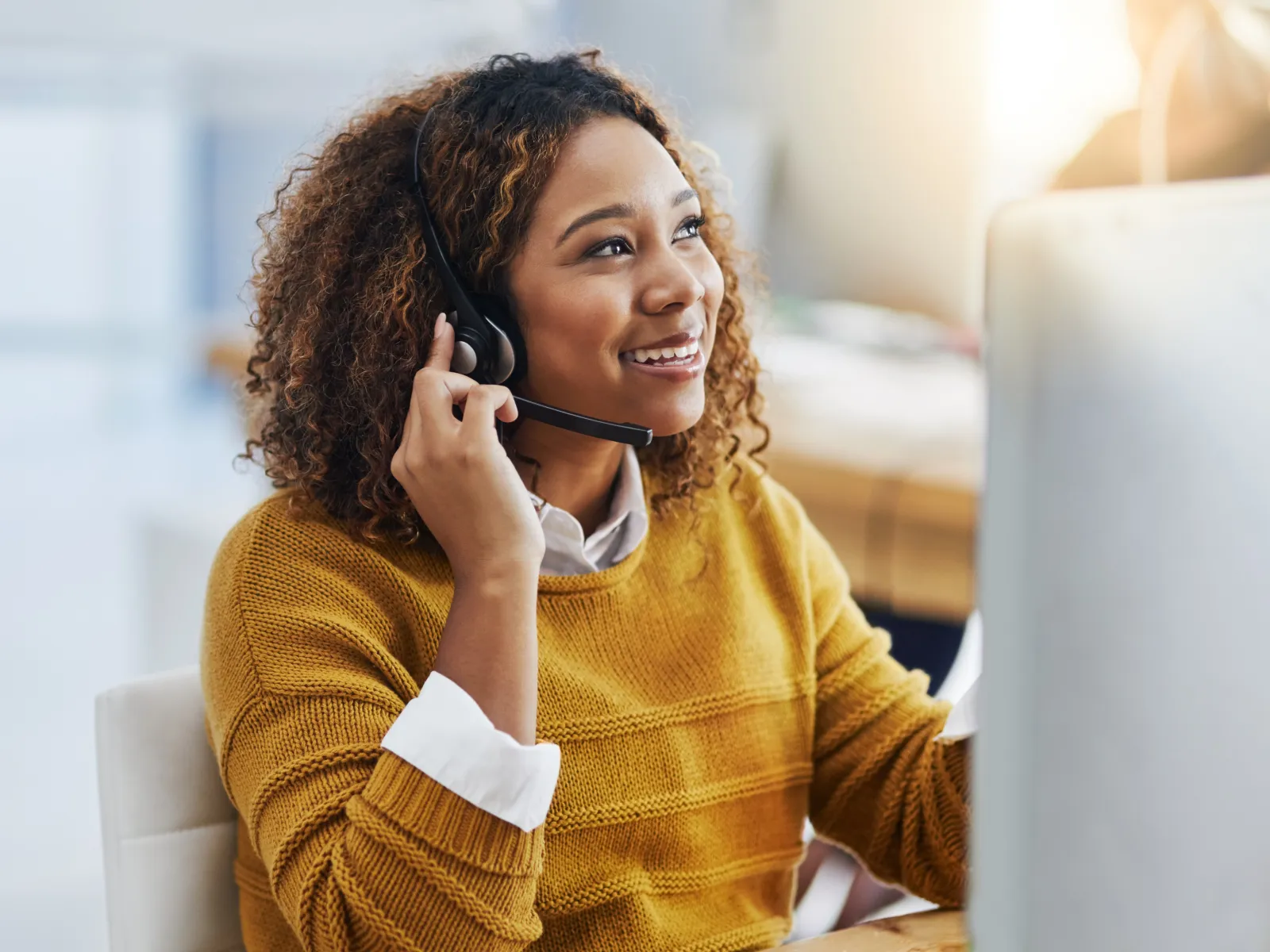 Smiling woman wearing headset works at computer in bright modern office environment