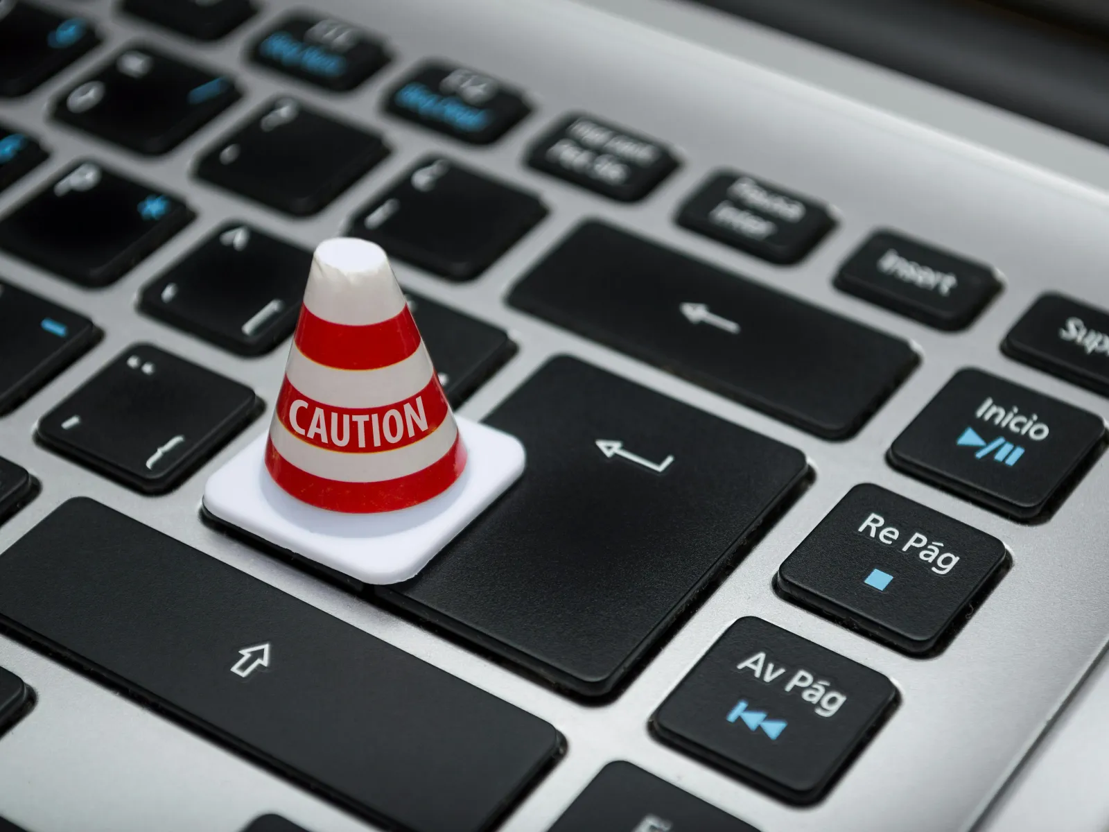 Mini caution cone placed on the enter key of a black and silver computer keyboard conveying a warning concept.