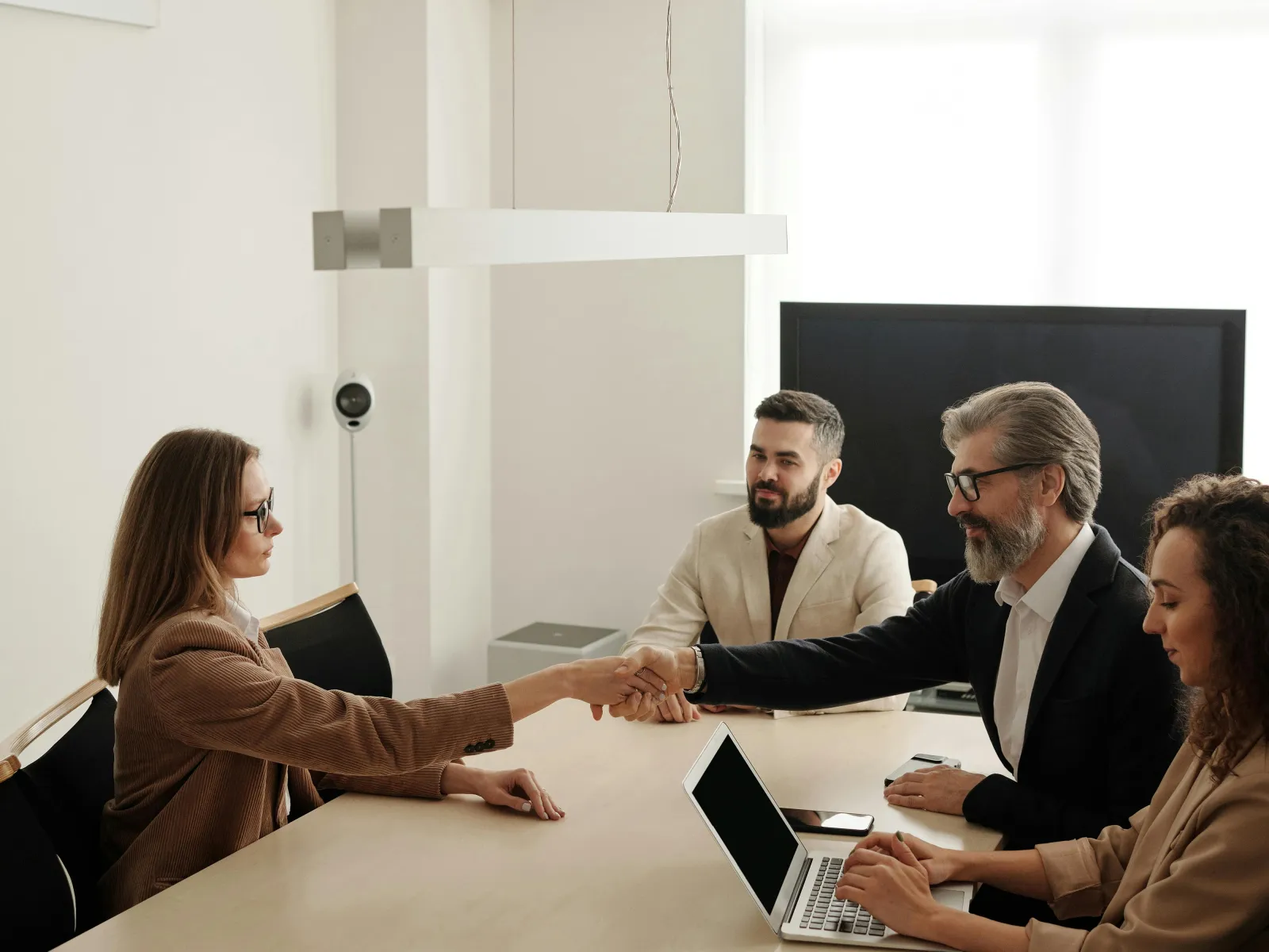 Business meeting with professionals shaking hands across a table in a modern office setting.