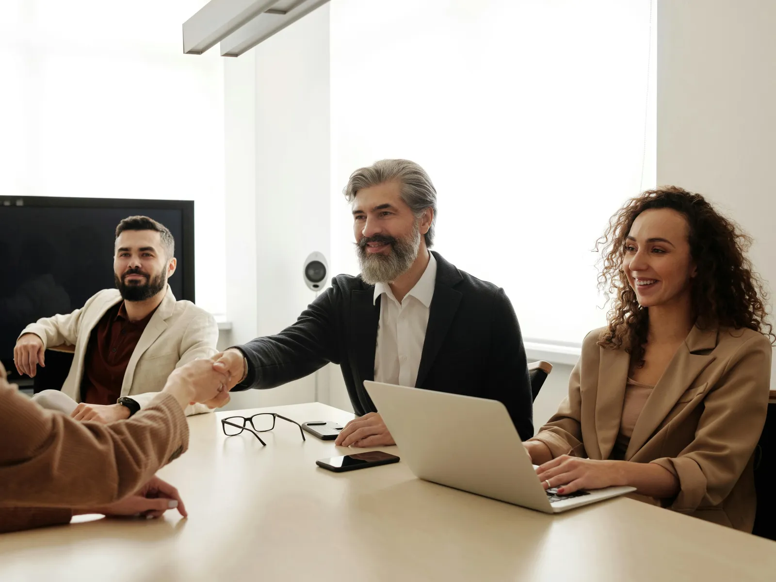 Business professionals shaking hands in a meeting room with laptops and smiles during a friendly discussion
