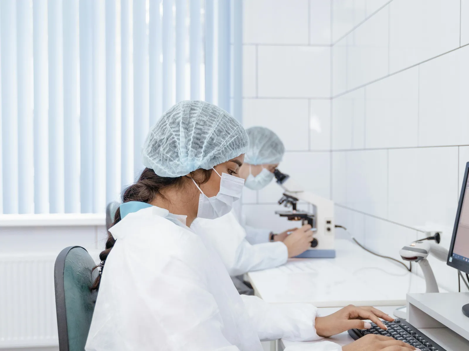 Two scientists in protective clothing working in a sterile lab with a computer and microscope