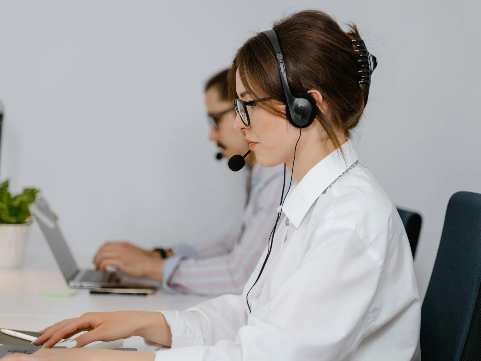 Customer service representatives wearing headsets working on laptops in a bright office environment.