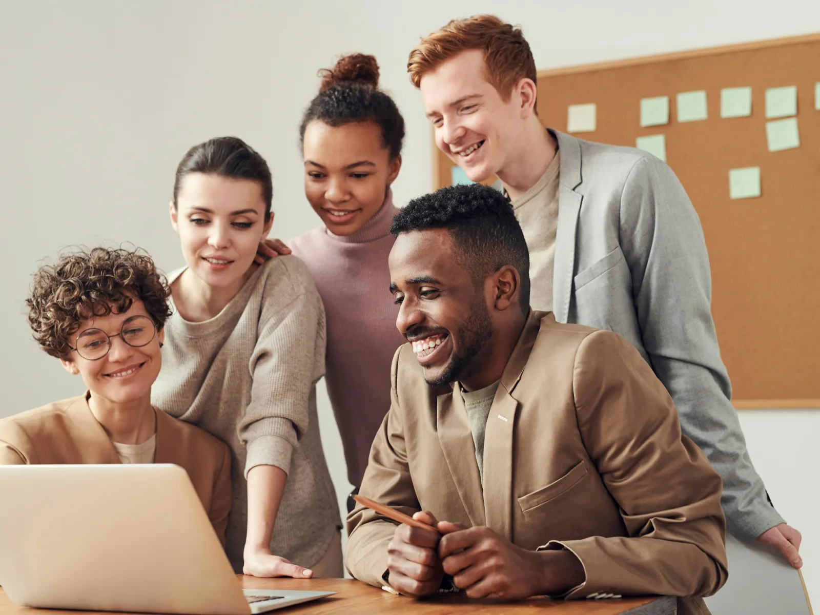 Diverse group of young professionals collaborating and smiling while looking at a laptop in an office.