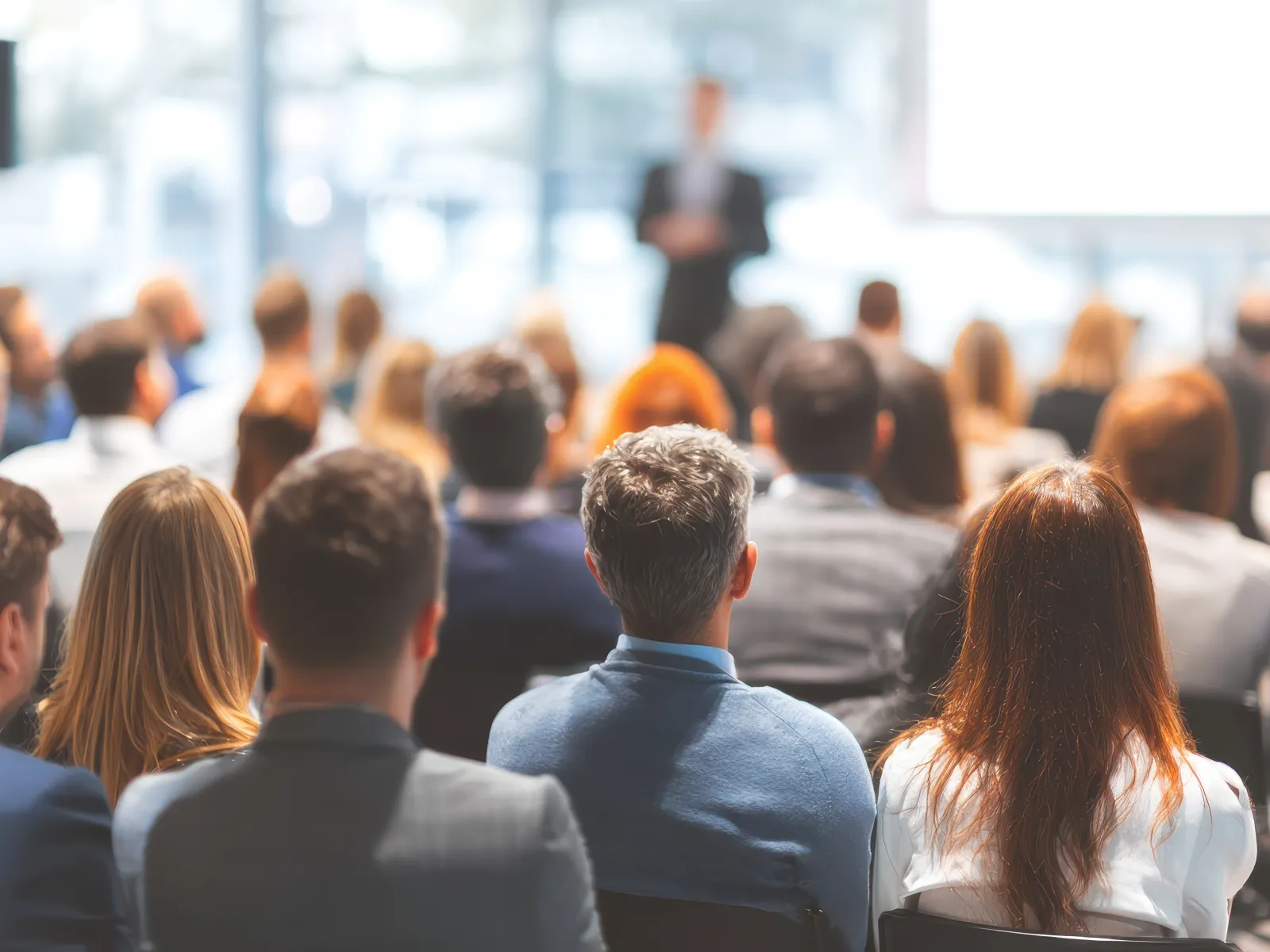 Audience listening to a speaker in a bright conference room during a business seminar or workshop.