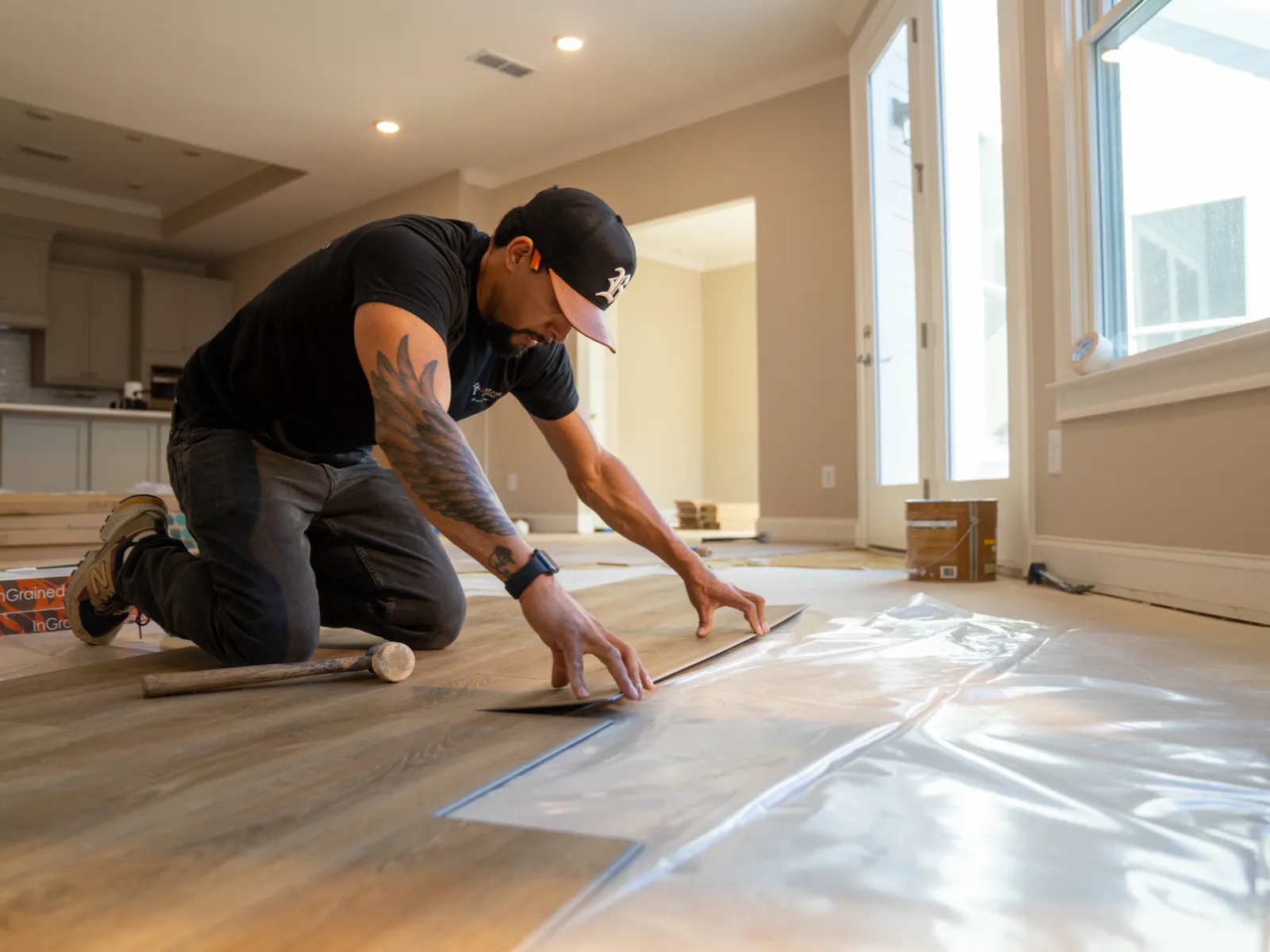 Worker installing vinyl plank flooring in a modern home, aligning planks on plastic underlayment.