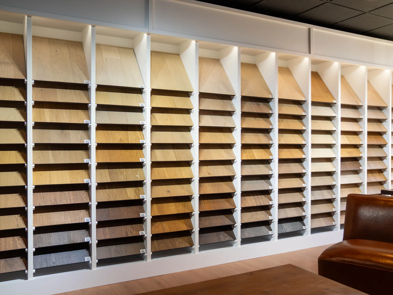 Wall display of various wood veneer samples in multiple shades with a leather chair and wooden table in foreground