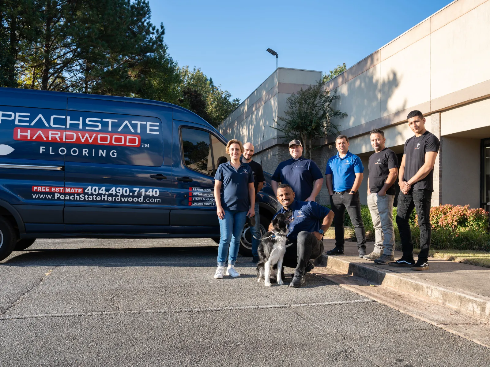 PeachState Hardwood Flooring team posing with a dog beside their branded service van outside a building on a sunny day.