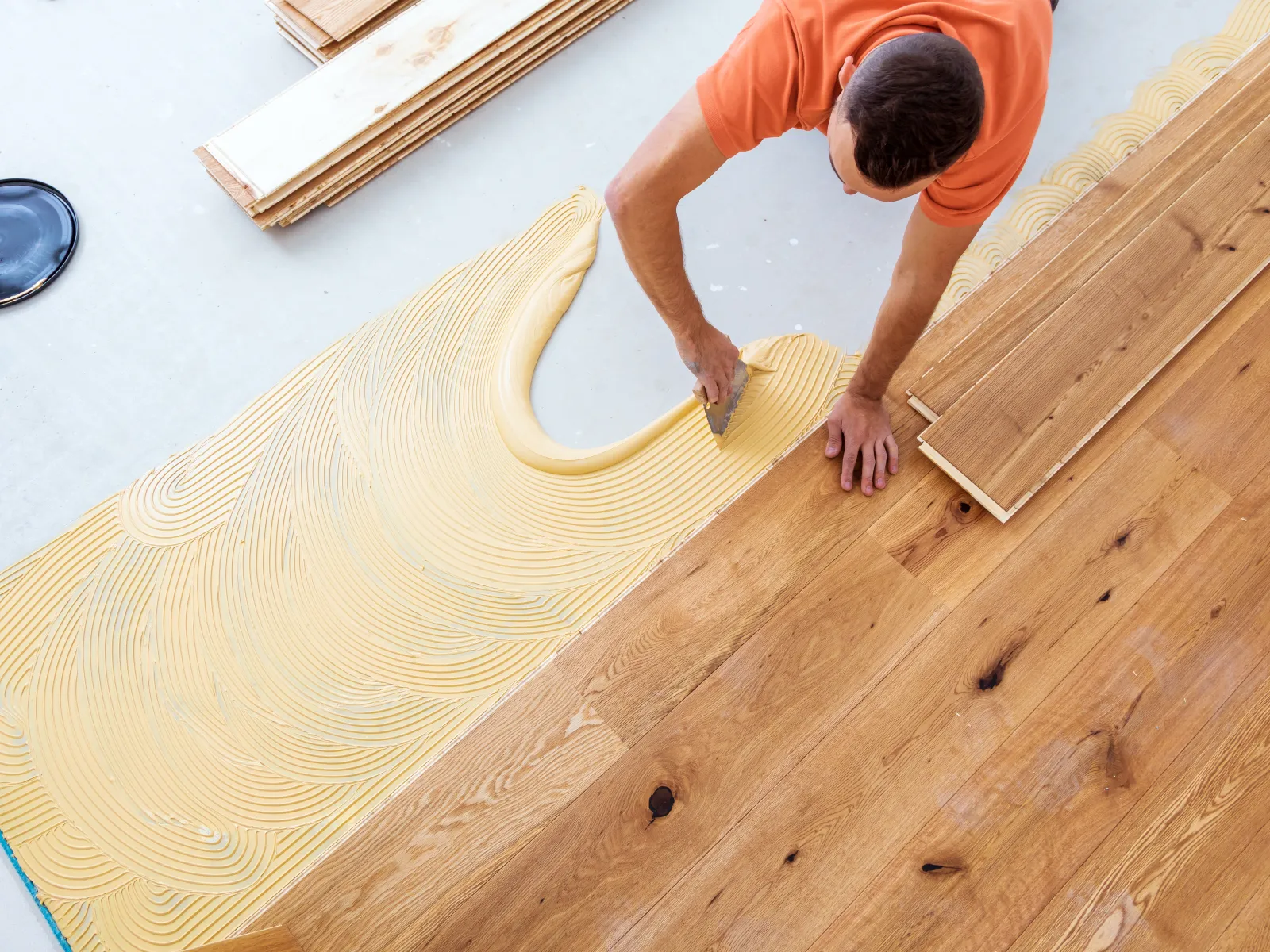 Worker installing wooden flooring with adhesive using a trowel for smooth application indoors