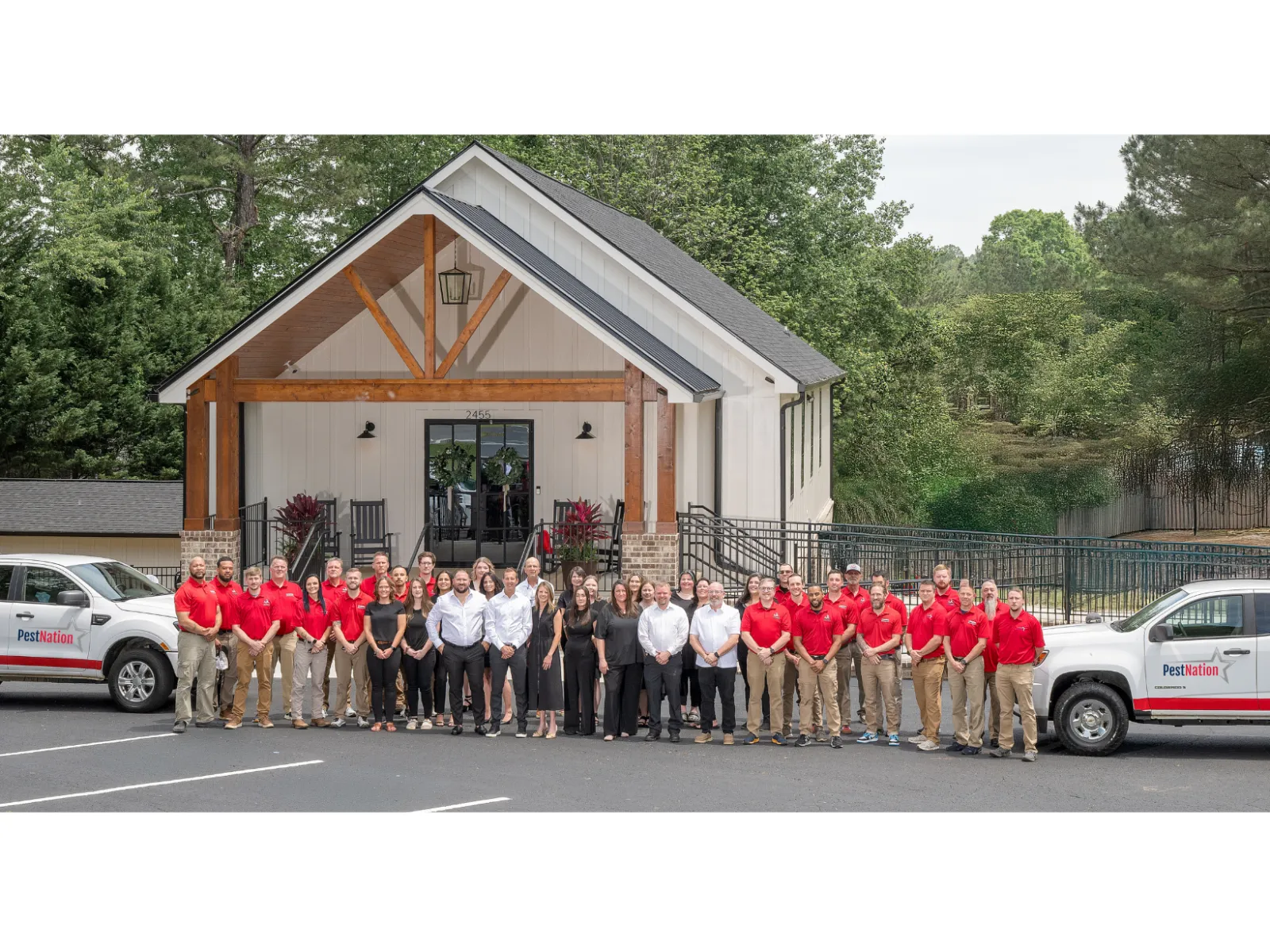 Large group of pest control professionals standing outside modern office building with branded company trucks.
