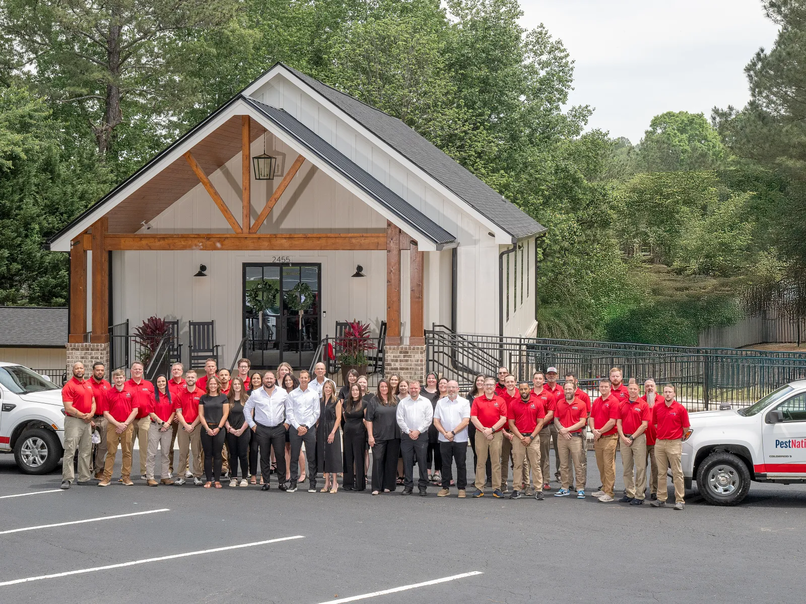 Large team of PestNation employees in red and black uniforms standing outside a modern office building with company trucks