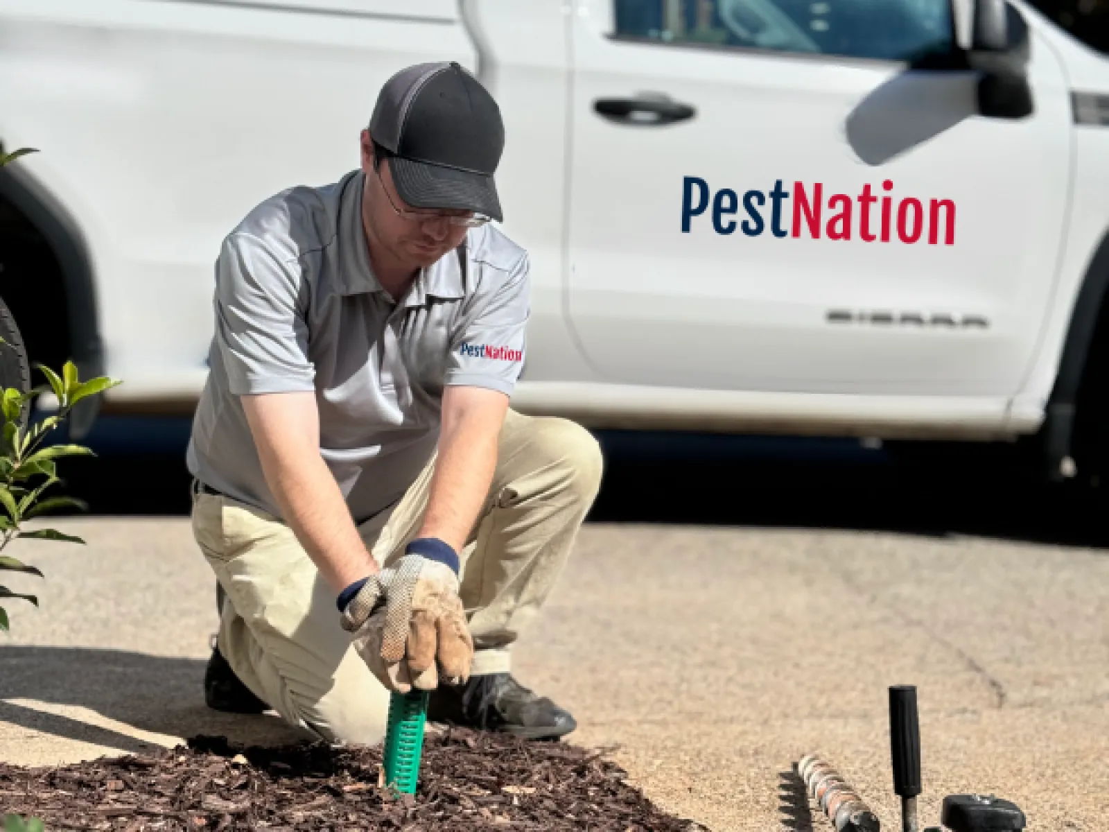 PestNation technician installing pest control equipment in a landscaped area.