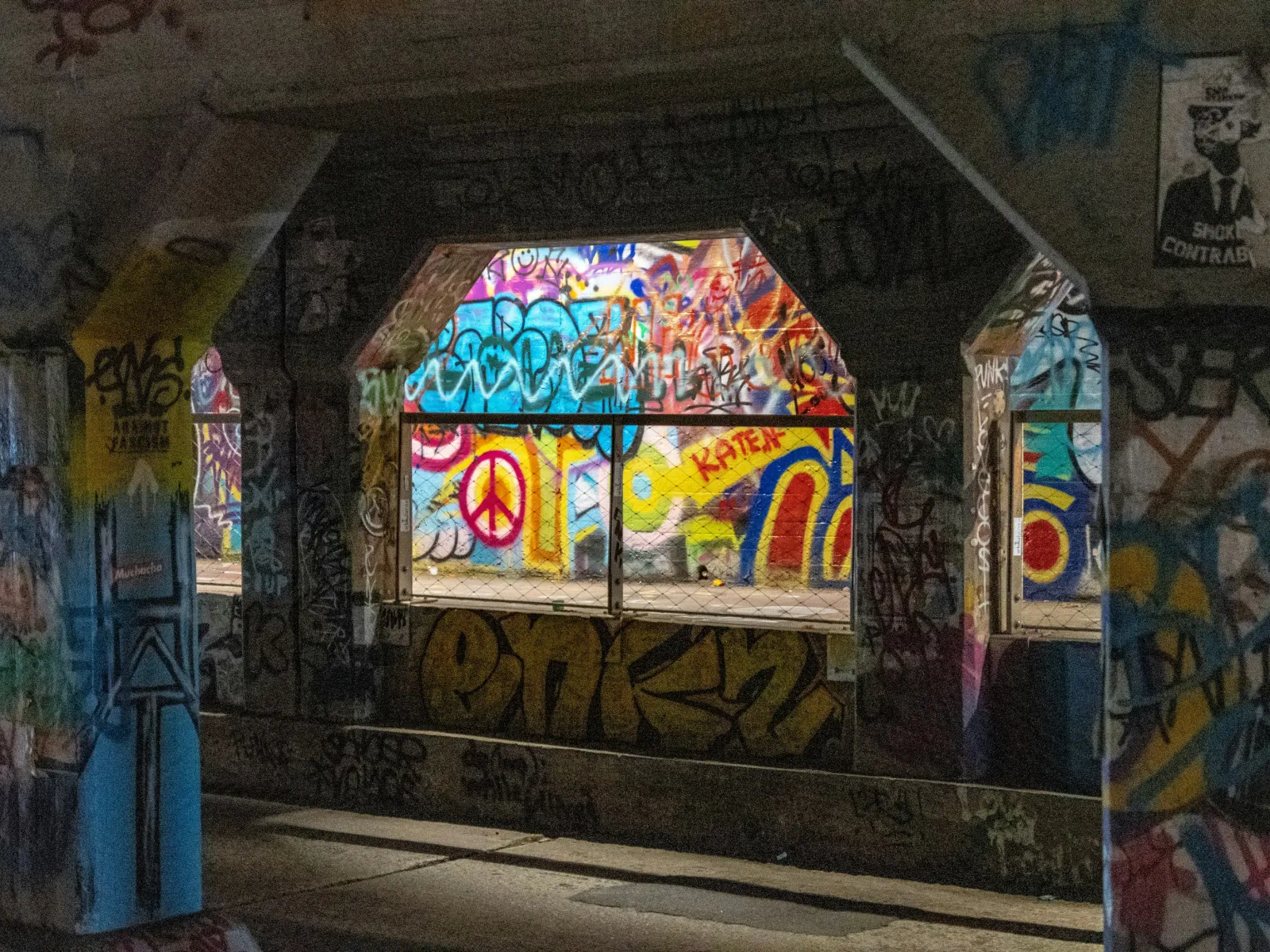 Colorful graffiti with peace sign seen through dark tunnel windows covered in street art and tags.