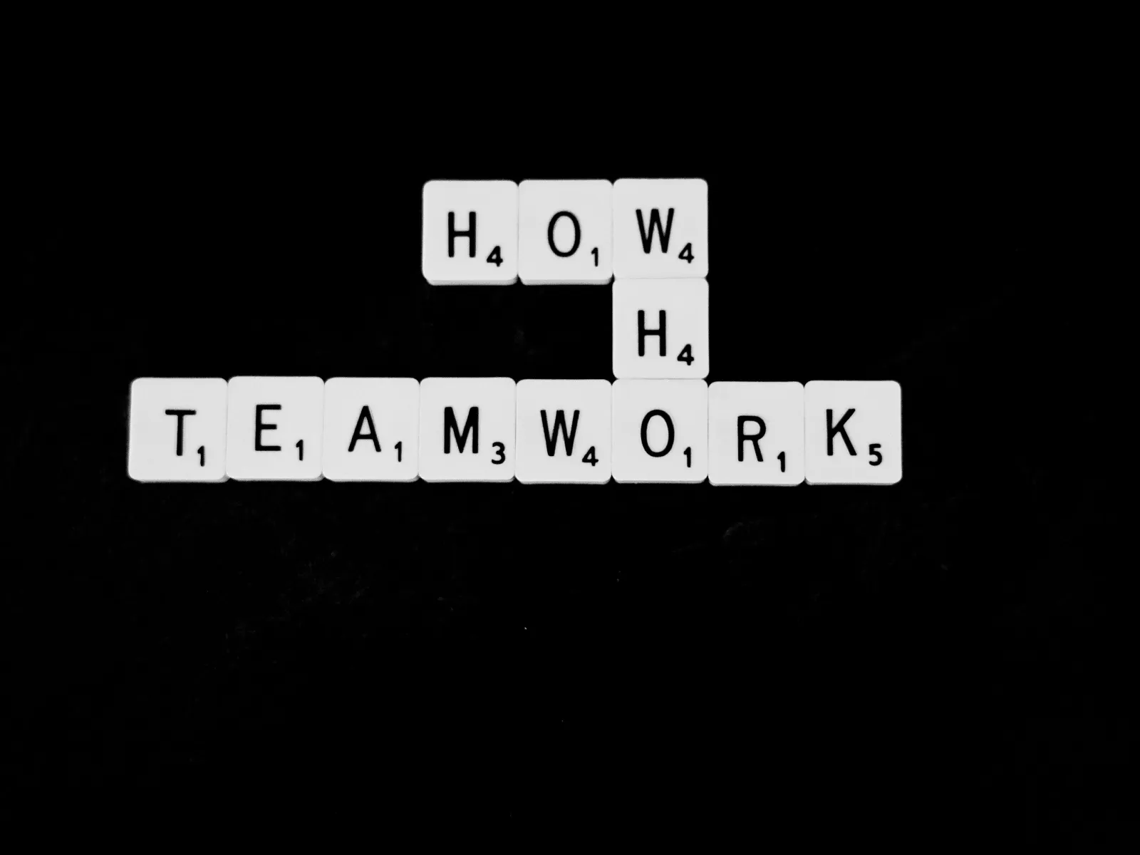 Scrabble tiles spell out the word 'TEAMWORK' on a black background, emphasizing collaboration and unity.
