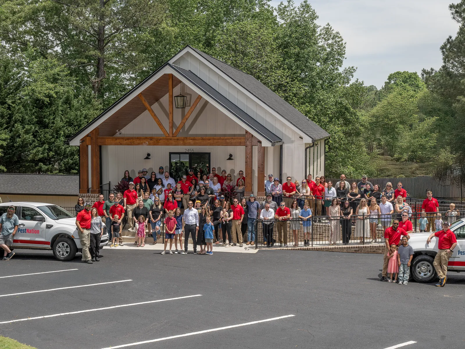 Large group of people posing outside a modern building with two Pest Nation trucks in a parking lot surrounded by trees