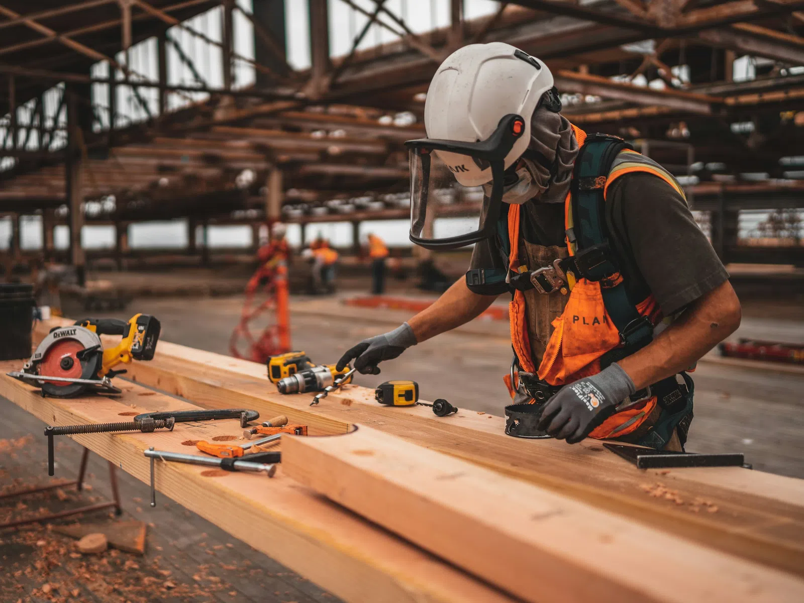 Carpenter in safety gear working with wood and power tools on a construction site with metal framework.