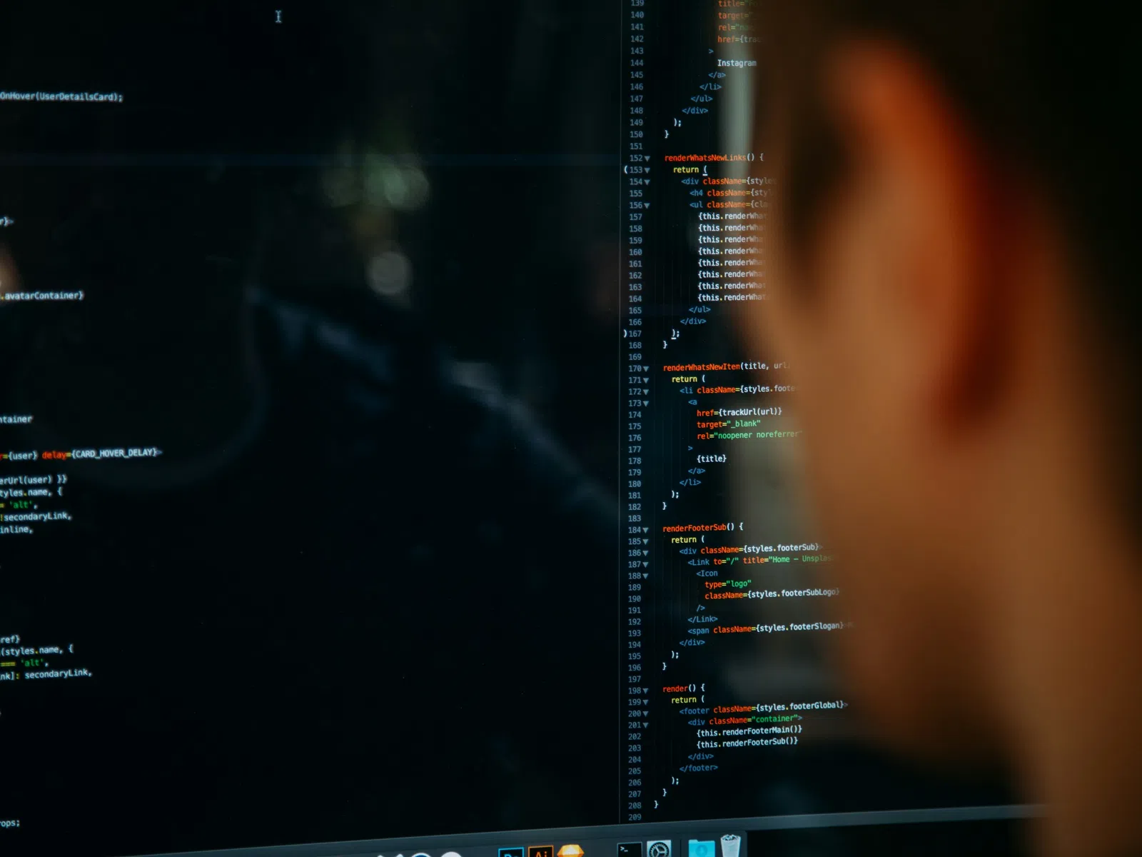 Developer viewing JavaScript code on a dark screen reflecting in a glass surface in a dimly lit room.