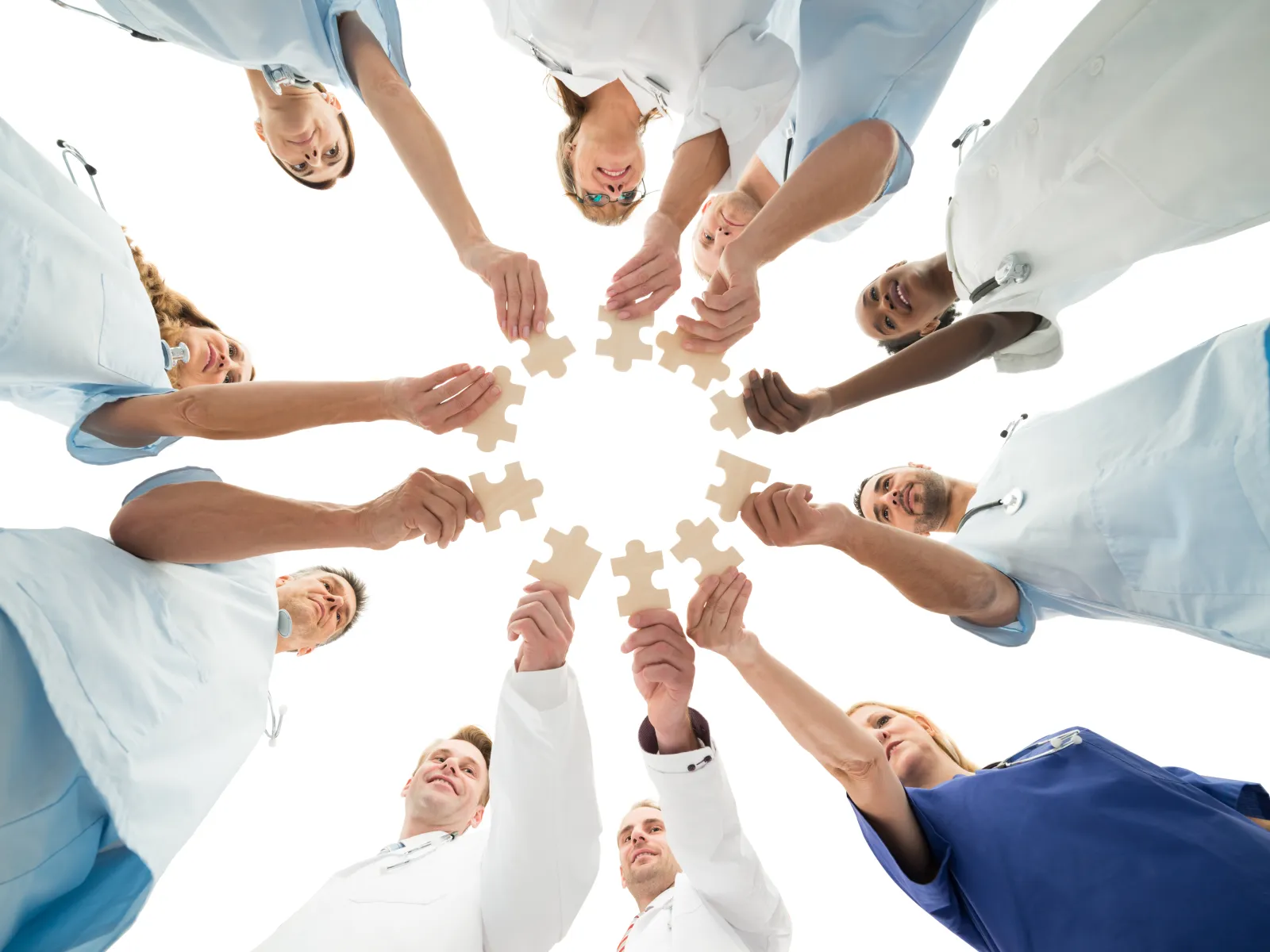 Healthcare professionals in scrubs and lab coats joining puzzle pieces in a circle representing teamwork and collaboration.