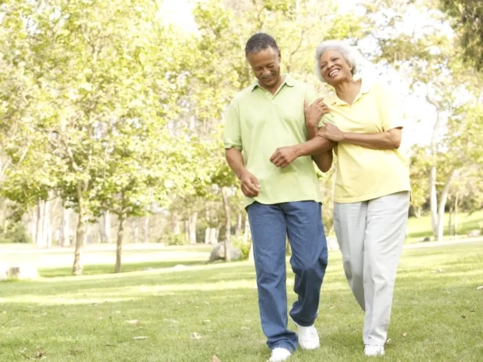 Senior couple walking arm in arm smiling happily in a sunny green park with trees in the background