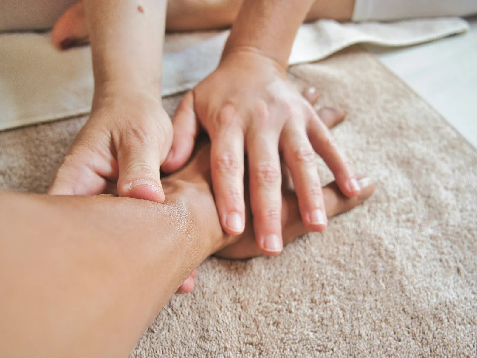 Hands performing a wrist massage on a person's arm over a beige towel in a relaxing setting