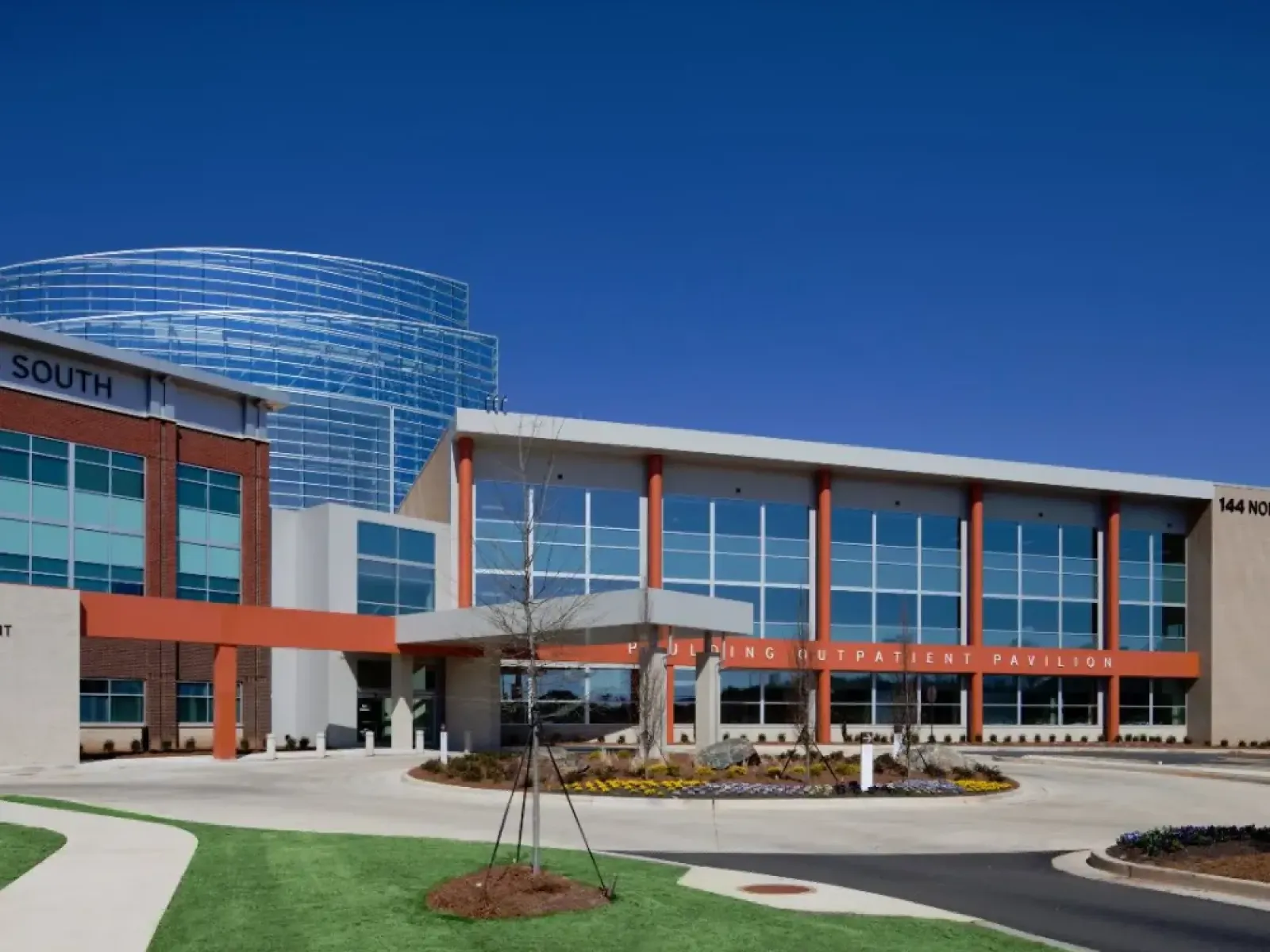 Modern outpatient pavilion with large windows and red accents under a clear blue sky at a medical facility.