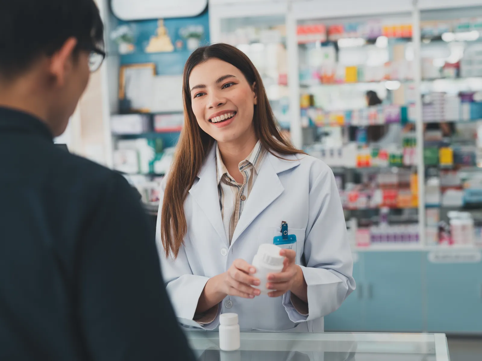Smiling female pharmacist in white coat advising customer about medication in a pharmacy setting.